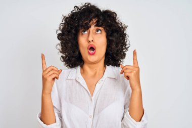 İzole beyaz arka plan üzerinde rahat gömlek giyen kıvırcık saçlı genç arap kadın şaşırttı ve yukarı bakarak ve parmakları ile işaret ve kolları kaldırdı şaşırttı.