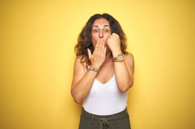 Orta yaş yaşlı kadın sarı izole arka plan kapağı ağız üzerinde bilek lik gösteren el hata için utanç ile şok, korku ifadesi, sessizlik, gizli kavram korkmuş