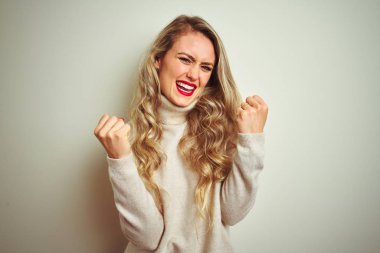 İzole beyaz arka plan üzerinde kış boğazlı kazak giyen güzel kadın kollarını kaldırdı ve gözleri kapalı ile başarı için sürpriz ve şaşırttı. Kazanan kavramı.