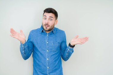 İzole arka plan clueless ve şaşkın bir ifadeyle kollar ve eller kaldırdı genç yakışıklı adam. Şüphe kavramı.