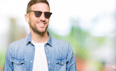 Yakışıklı adam uzak tarafına gülümseme ile yüzünde, doğal ifade arıyorum moda güneş gözlüğü takıyor. Kendine güvenen gülüyor.