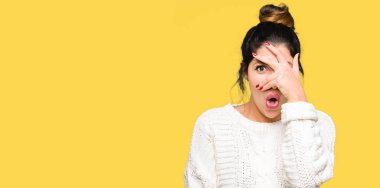 Mahcup ifadeyle parmaklarımın arasından seyir yüz ve gözler el ile kapsayan şok kazak kış bakmak giyen genç güzel kadın.