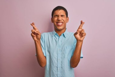 İzole pembe arka plan gesturing parmak üzerinde duran mavi gömlek giyen genç yakışıklı Arap adam umut ve gözleri kapalı gülümseyerek geçti. Şans ve batıl kavram.