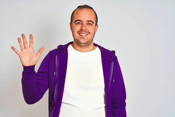 孤立した白い背景の上に立つ紫色のスウェットシャツを着た若い男性は 自信を持って幸せに微笑みながら 指番号5を示し 指を上げている — ストック写真