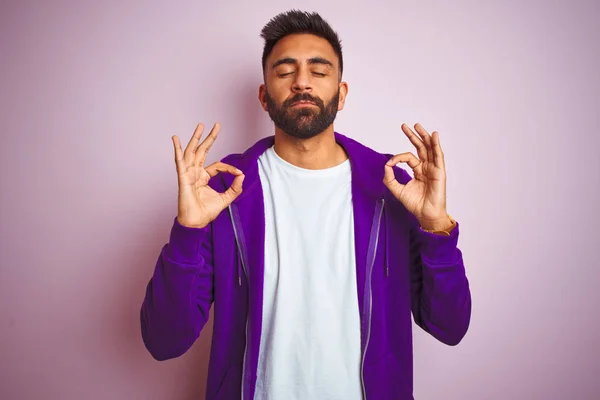 年轻的印度男子穿着紫色运动衫站在孤立的粉红色背景放松和微笑与眼睛闭着手指做冥想手势 瑜伽概念 — 图库照片