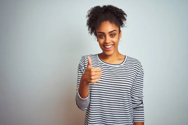 African american woman wearing navy striped t-shirt standing over isolated white background doing happy thumbs up gesture with hand. Approving expression looking at the camera showing success.