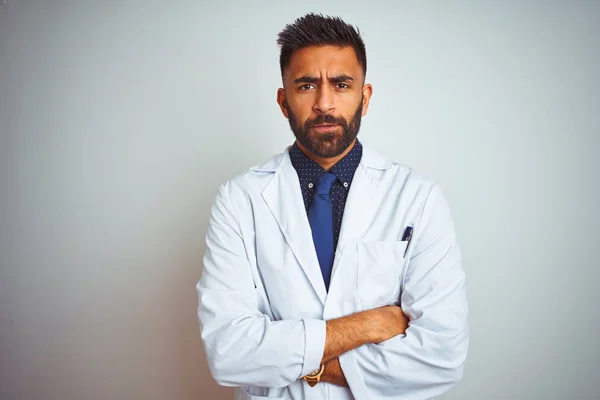 Young indian doctor man standing over isolated white background skeptic and nervous, disapproving expression on face with crossed arms. Negative person.