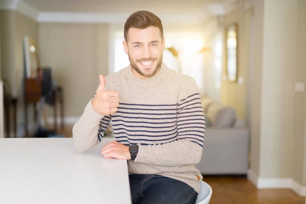 年轻的帅哥穿着毛衣在家里做快乐的竖起大拇指手势与手 批准表达式 以显示成功的相机 — 图库照片