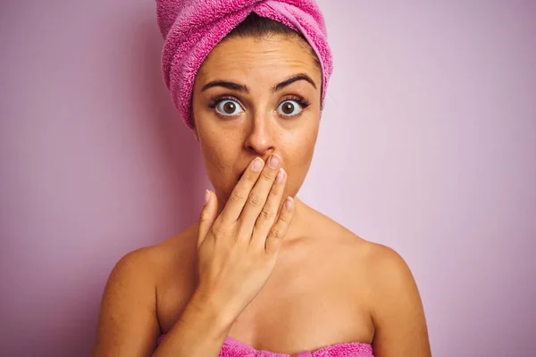 Young beautiful woman wearing towel after shower over isolated pink background cover mouth with hand shocked with shame for mistake, expression of fear, scared in silence, secret concept