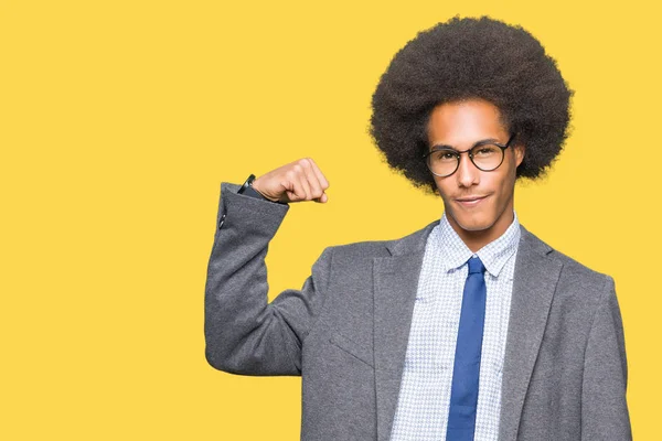 Young african american business man with afro hair wearing glasses Strong person showing arm muscle, confident and proud of power