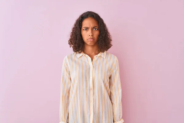 Young brazilian woman wearing striped shirt standing over isolated pink background skeptic and nervous, frowning upset because of problem. Negative person.