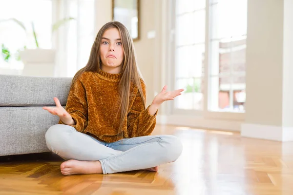 Ev clueless ve kollar ve elleri ile karıştı ifade yerde oturan güzel genç kız çocuk kaldırdı. Şüphe kavramı.