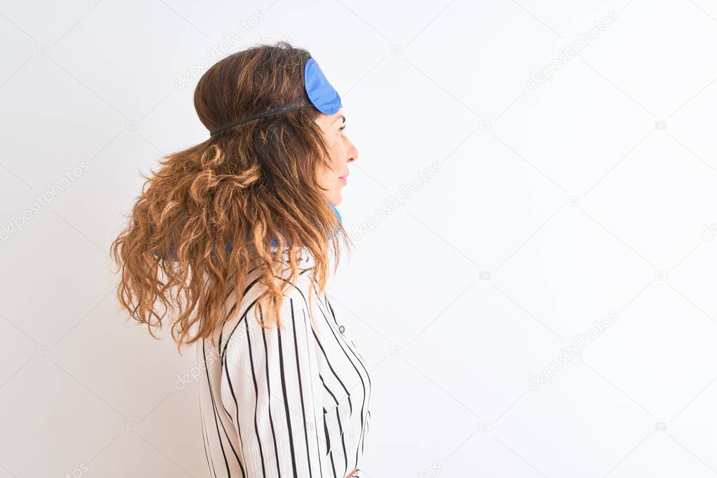 Middle age tourist woman wearing neckpillow and sleep mask over isolated white background looking to side, relax profile pose with natural face with confident smile.