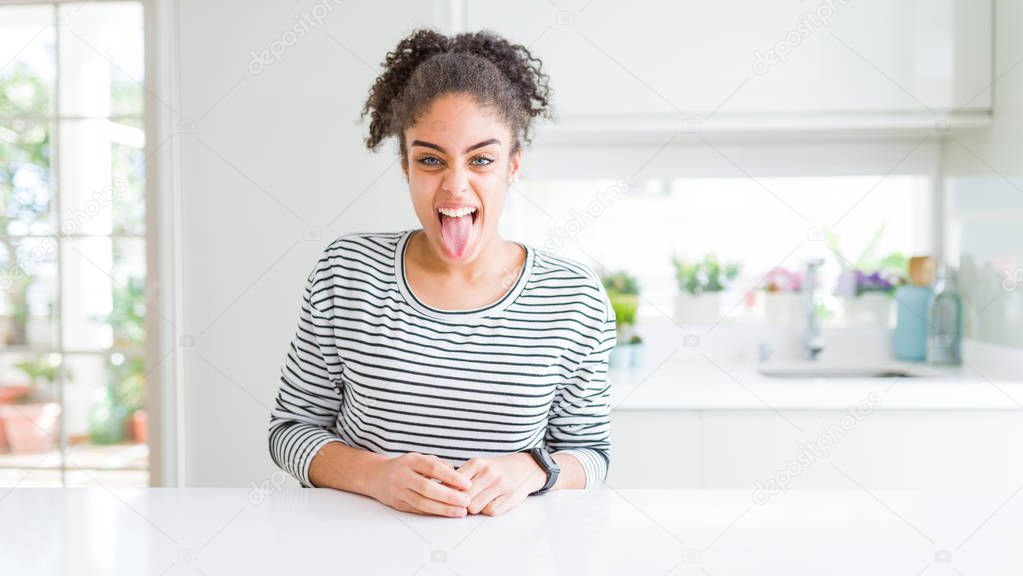 Beautiful african american woman with afro hair wearing casual striped sweater sticking tongue out happy with funny expression. Emotion concept.