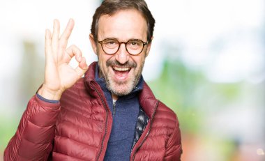 Gözlük ve kış ceket el ve parmaklar ok işaretiyle yapıyor olumlu gülümseyen giyen orta yaş yakışıklı adam. Başarılı ifade.
