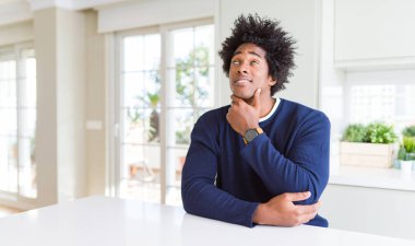 Genç afro-amerikan adam gündelik kazak giyen evde eliyle çenesi üzerinde oturan soru, dalgın ifade düşünme. Gülümseyen ve düşünceli bir yüz. Şüphe kavramı.