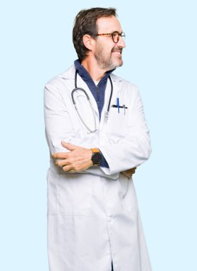 Yüz, doğal ifade gülümseme ile kenara bakıyor tıbbi ceket giyen yakışıklı orta yaş Doktor adam. Güven gülüyor.