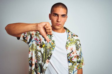 Tatilde beyaz arka plan üzerinde Hawaii gömlek giyen genç yakışıklı adam mutsuz ve kızgın gösteren reddi gösteren ve aşağı jest başparmak ile negatif. Kötü ifade.
