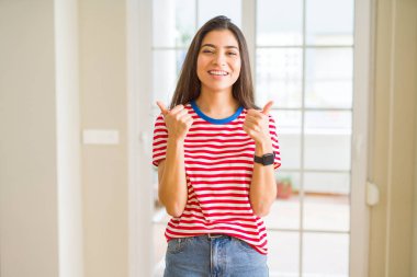 El ile olumlu hareketi yaparken rahat t-shirt başarı işareti giyen genç güzel kadın başparmak gülümseyen ve mutlu. Neşeli bir ifadeyle, kazanan jest kameraya bakıyor.