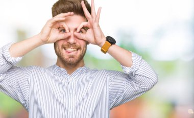 Genç yakışıklı adam, dürbün gibi jest yapıyor. Dilini çıkarıyor, gözleri parmaklarından bakıyor. Çılgın ifade.