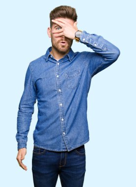 Mahcup ifadeyle parmaklarımın arasından seyir rahat kot gömlek yüz ve gözler el ile kapsayan şok bakmak giyen genç sarışın yakışıklı.