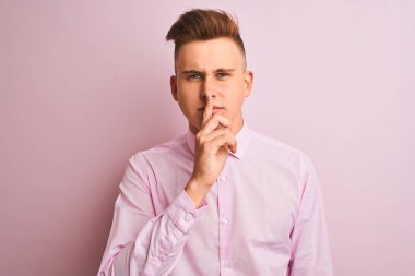 Genç yakışıklı işadamı dudaklarında parmak ile sessiz olmak isteyen izole pembe arka plan üzerinde duran zarif gömlek giyiyor. Sessizlik ve gizli kavram.