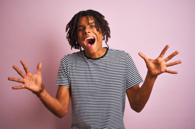 Dreadlocks giyen dreadlocks ile lacivert çizgili t-shirt izole pembe arka plan üzerinde deli kutluyor ve silah kaldırdı ve açık gözleri ile başarı için hayran heyecanlı çığlık giyen. Kazanan kavramı