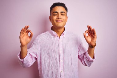 Genç Brezilyalı adam izole pembe arka plan üzerinde duran gömlek giyen rahatlayın ve gözleri parmakları ile meditasyon jest yapıyor kapalı gülümseyerek. Yoga konsepti.