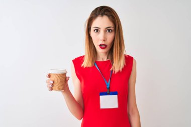 İzole beyaz arka plan üzerinde kahve içen kimlik kartı giyen kızıl saçlı iş kadını sürpriz bir yüz ile şok korkmuş, korku ve korku ifade ile heyecanlı