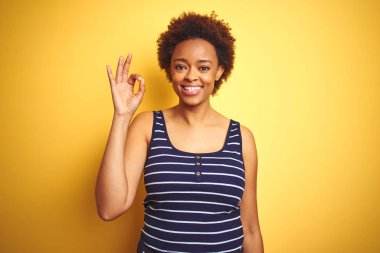 Beauitul Afrikalı Amerikan kadın izole sarı arka plan üzerinde yaz t-shirt giyen olumlu el ve parmaklar ile ok işareti yapıyor. Başarılı ifade.