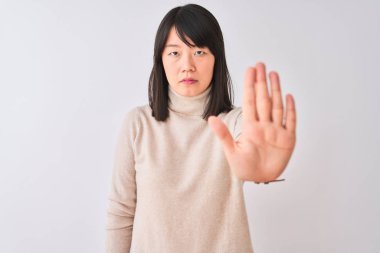 Genç güzel Çinli kadın izole beyaz arka plan üzerinde balıkçı yaka kazak giyen avuç içi ile şarkı durdurmak yapıyor. Yüzünde olumsuz ve ciddi bir jest olan uyarı ifadesi.