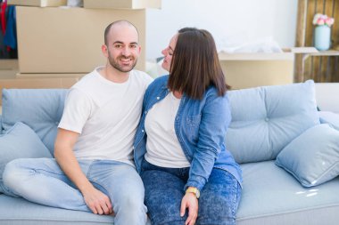 Aşk rahatlatıcı ve yeni bir evde kanepede oturan sarılmak genç çift, yeni bir daireye taşınmak için çok mutlu gülümseyen