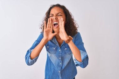 İzole beyaz arka plan üzerinde duran denim gömlek giyen genç Brezilyalı kadın ağız üzerinde elleri ile yüksek sesle kızgın bağırarak