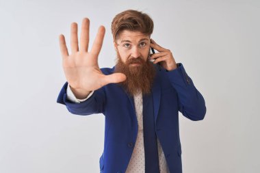 Genç kızıl saçlı İrlandalı işadamı ciddi ve kendinden emin ifade, savunma jesti ile dur işareti yapıyor açık el ile izole beyaz arka plan üzerinde akıllı telefon konuşuyor