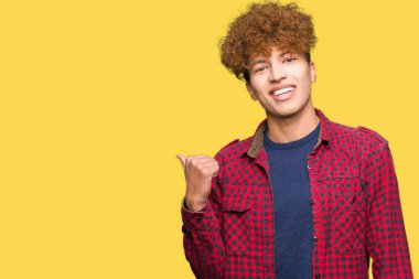 Afro saçlı genç yakışıklı öğrenci adam mutlu yüz görünümlü gülümseyen bir ceket giyen ve başparmak ile yan işaret.