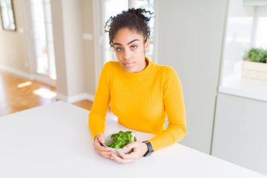 Genç afro-amerikan kız ciddi düşünme akıllı yüz kendine güvenen bir ifade ile heatlhy yeşil brokoli yeme