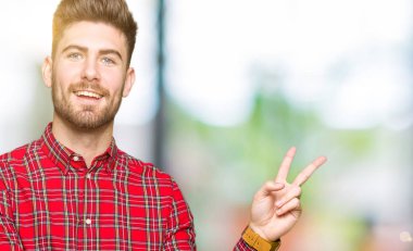 Genç, yakışıklı, gülümseyen ve kameraya göz kırpan bir adam zafer işareti yapıyor. İki numara..