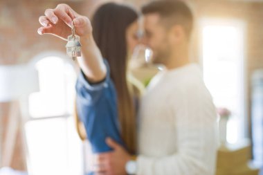 Genç çift yeni bir eve hareket, yeni dairenin anahtarlarını gösteren aşk sarılmak çok mutlu gülümseyen