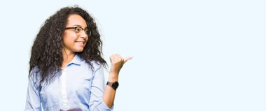 Kıvırcık saçlı Genç güzel iş kızı görünümlü ve başparmak yukarı ile yan işaret mutlu yüz ile gülümseyen gözlük giyiyor.