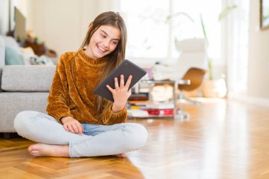 Dijital touchpad tablet kullanan güzel genç kız çocuk mutlu bir yüz le yerde otururken ayakta ve dişleri gösteren kendinden emin bir gülümseme ile gülümseyerek