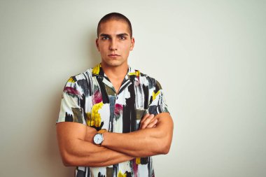 Beyaz izole arka plan şüpheci ve sinir üzerinde yazlık gömlek giyen genç yakışıklı adam, çapraz kolları ile yüzünde ifade onaylamayan. Negatif kişi.