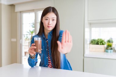Güzel Asyalı kadın ciddi ve kendinden emin ifade, savunma jesti ile durdurmak işareti yapıyor açık el ile çikolata milkshake taze bir bardak içme