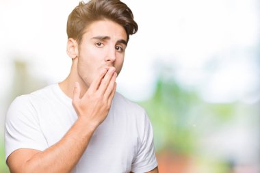 Yakışıklı delikanlı izole arka plan üzerinde beyaz t-shirt giyen el ağzıyla kapsayan yorgun esneme sıkılmış. Restless ve uyku hali.