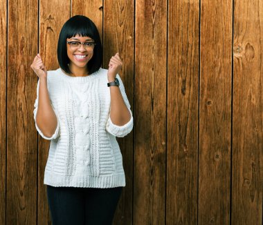 Güzel genç Afro-Amerikan kadın izole arka plan üzerinde kutluyor gözlük takan şaşırttı ve silah ile başarı için yükseltilmiş ve açık gözler hayrete düşürdü. Kazanan kavramı.