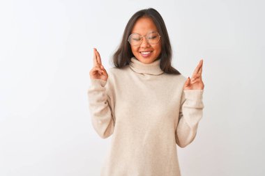 Genç çinli kadın boğazlı kazak ve gözlük izole beyaz arka plan gesturing parmak üzerinde umut ve gözleri kapalı gülümseyerek geçti giyen. Şans ve batıl kavram.