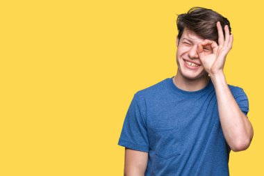 Gülümseyen, parmakları ile mutlu yüz üzerinden seyir göz el ile ok jest yapıyor izole arka plan üzerinde mavi t-shirt giyen genç yakışıklı adam.