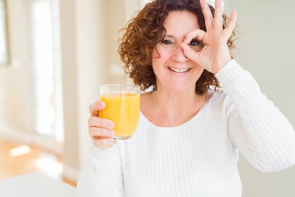 高级妇女滴着一杯新鲜的橙汁与快乐的脸微笑做确定的标志与手在眼睛通过手指看 — 图库照片