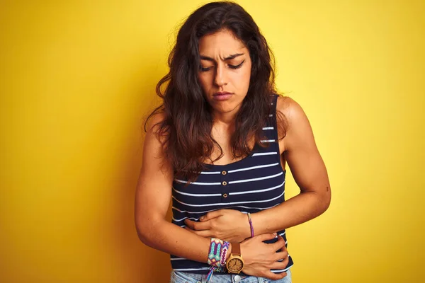 年轻美丽的女人穿着条纹T恤站在孤立的黄色背景与手在胃 因为消化不良 痛苦的疾病感觉不适 疼痛概念 — 图库照片