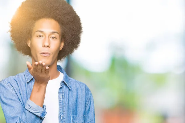 Young african american man with afro hair looking at the camera blowing a kiss with hand on air being lovely and sexy. Love expression.
