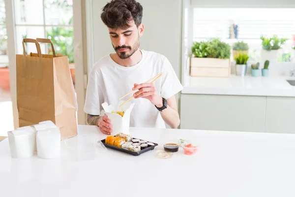 Young man eating sushi asian food and noodles using choopsticks